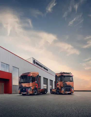 Two Renault Trucks T High tractor units are parked in front of a Renault Trucks dealership at dusk.